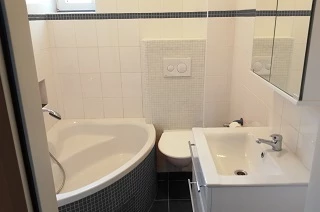Standardní toaleta v nájemním bytě - závěsná toaleta, moderní umyvadlo, rohová vana, skříňka pod umyvadlem, skříňka nad umyvadlem